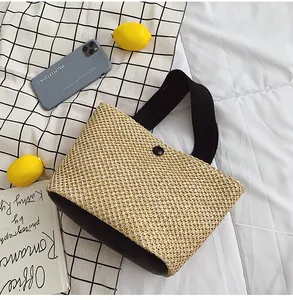 Overhead view of a woven straw handbag with black fabric handles and a snap button closure