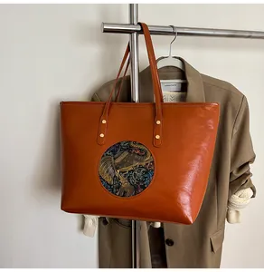 Detail of the elephant embossed emblem on a polished caramel leather tote bag