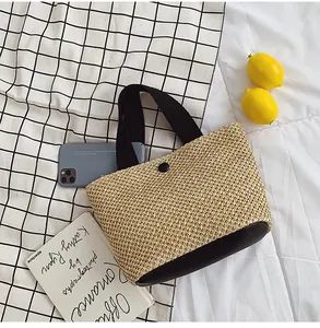 Detailed top view of a woven straw handbag featuring black handles and a button closure