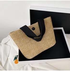 Detailed weave of straw tote bag with black strap and central button on a gift box