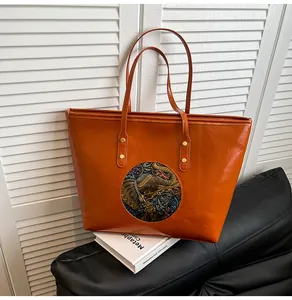 Detail of orange tote bag featuring an embossed ethnic elephant badge and gold rivets