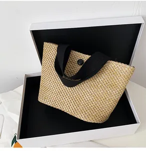 Detail of hand-woven straw beach bag featuring black handle and metal snap closure