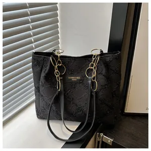 Detail of black textured tote bag with golden chain rings and fashion brand label