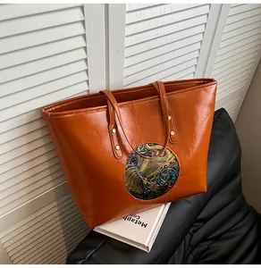 Detail of embossed ethnic elephant patch on brown leather tote with gold rivets