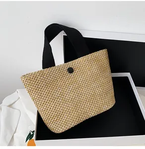 Detailed close-up of handmade woven straw tote with black fabric handles and button closure