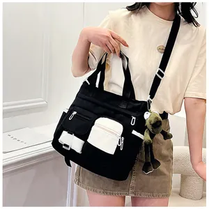 Detail of a black canvas tote bag featuring multi-pocket utility design and a frog pendant