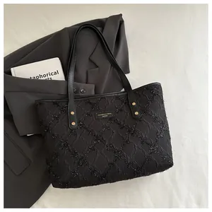 Detail of black quilted tote bag with metallic logo plate and gold rivet handles