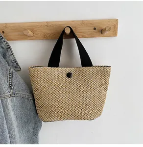 Detail of woven straw handbag texture with black handles and button on white wall hook