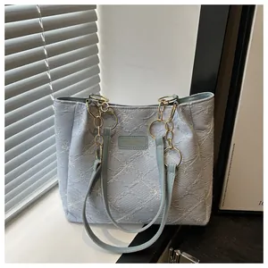 Detailed embroidery of white flowers on a light blue tote bag with gold chain strap