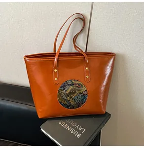 Close-up of caramel tote bag featuring embossed colorful elephant motif and gold metal rivets