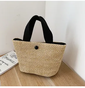 Detail of hand-woven straw bag featuring black ribbon handles and secure magnetic closure