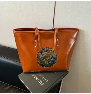 Detailed view of embossed elephant totem and golden rivet studs on caramel tote bag