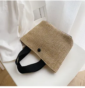Detailed close-up of woven straw handbag with black straps on a white chair