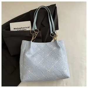 Detail of light blue quilted tote bag with floral embroidery and golden chain strap