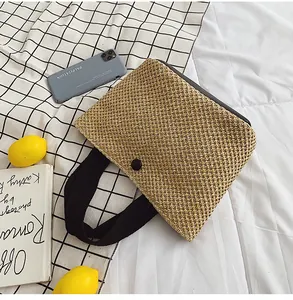 Close-up of woven straw handbag featuring black textured handles and round button detail