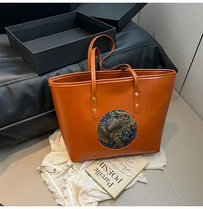 Detailed view of an orange leather tote bag with a colorful embossed elephant totem pattern