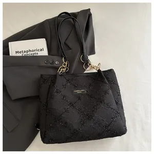 Detail of black textured tote bag featuring gold chain strap and brand label on surface
