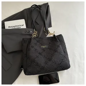 Macro view of black tweed tote bag texture with metal logo plate and chain strap