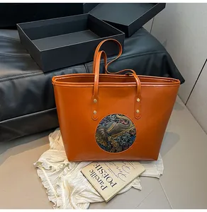 Detail of orange-brown tote bag with colorful elephant relief and golden rivets