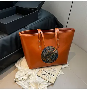 Detailed view of an orange leather tote bag featuring a round elephant pattern embossing