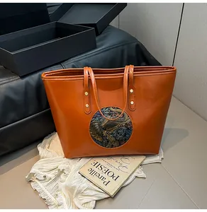 Detail of orange brown tote bag featuring a round embossed elephant pattern and gold studs