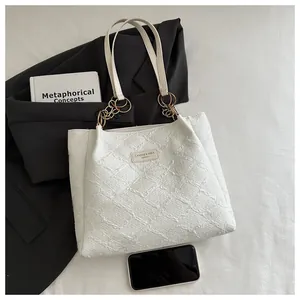 Detailed macro view of white textured tote bag with golden chain and phone for size reference