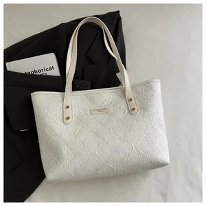 Close-up of white quilted tote bag featuring gold rivets and elegant brand name plate