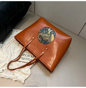 Detail of caramel brown leather tote bag featuring a colorful ethnic elephant emblem