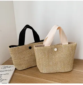Detail of small straw woven handbags with fabric handles and button closure on wood desk