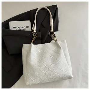 Close-up of white embossed tote bag with gold chain strap detail on minimalist background