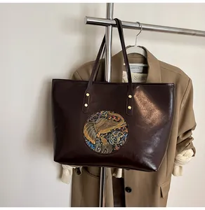 Detailed view of the dark brown leather tote bag with embossed golden elephant pattern