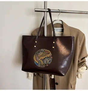Detailed view of dark brown leather tote with large circular elephant relief and scrollwork