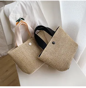 Detail of woven straw tote bags in beige and yellow with button closure on a white chair