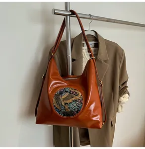 Close-up of brown leather tote bag with golden elephant relief emblem on shoulder strap