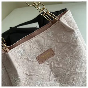 Detailed macro view of light pink floral embroidery and gold chain on a pleated tote bag