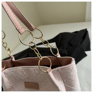 Macro view of textured light pink tote bag with bow embroidery and gold chain handle
