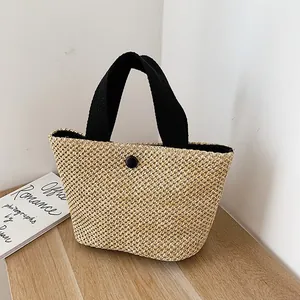 Handwoven straw beach bag with contrasting black handles and decorative button