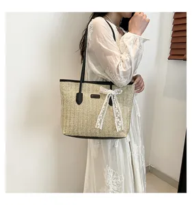 Détail du sac cabas en paille avec nœud en dentelle porté sur une robe d'été fleurie blanche