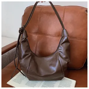 Detailed view of dark brown dumpling bag with pleated texture and decorative shoulder knot