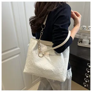 Detail of white tote bag featuring embossed texture fabric and elegant gold chain strap
