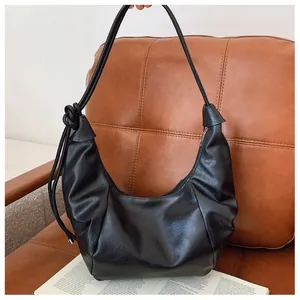 Close-up of black pleated PU leather hobo bag with knot detail on brown sofa background