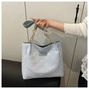 Detail of light blue quilted tote bag with floral embroidery and chain handle