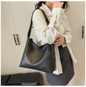 Model wearing a large black matte leather tote bag with a wide shoulder strap in a studio