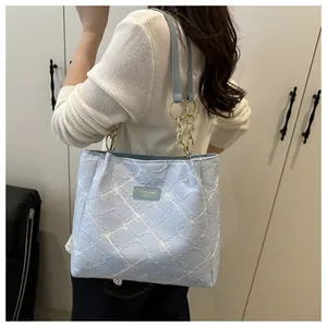 Detail of light blue quilted tote bag featuring white floral embroidery and chain strap