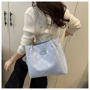 Detail of light blue tote bag with floral texture and gold chain strap shown on model