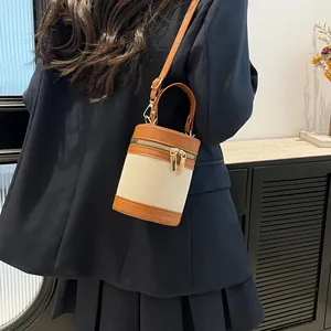Close-up of contrast stitching on canvas bucket bag with dual gold zippers and leather handle