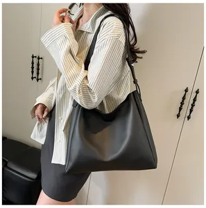 Minimalist black leather tote bag shown on shoulder in a modern indoor lifestyle setting
