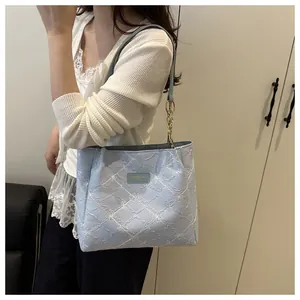 Close-up of light blue quilted tote with white floral embroidery and gold chain strap