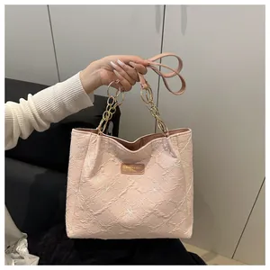 Detail of pink embroidered tote bag with golden chain strap and leather logo patch