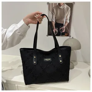 Close-up of black textured tote bag with gold brand plaque and metallic stud details